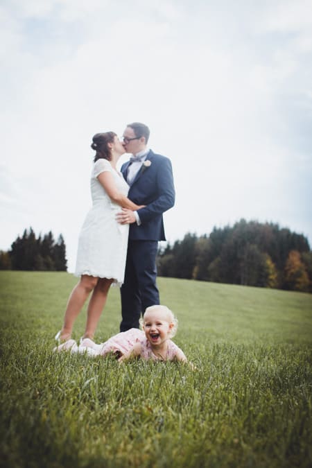 Brautpaar küsst sich. Im Vordergrund liegt die Tochter auf der Wiese